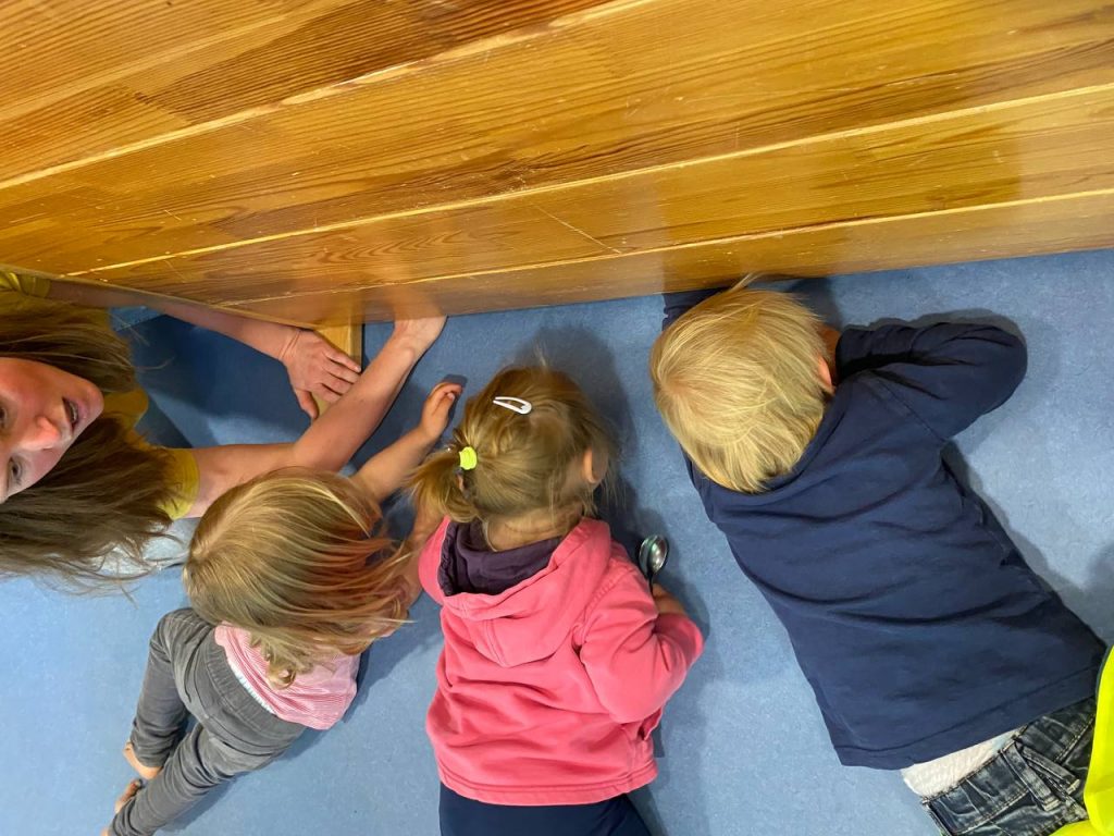 Drei Kinder schauen unter einen Holzkasten.